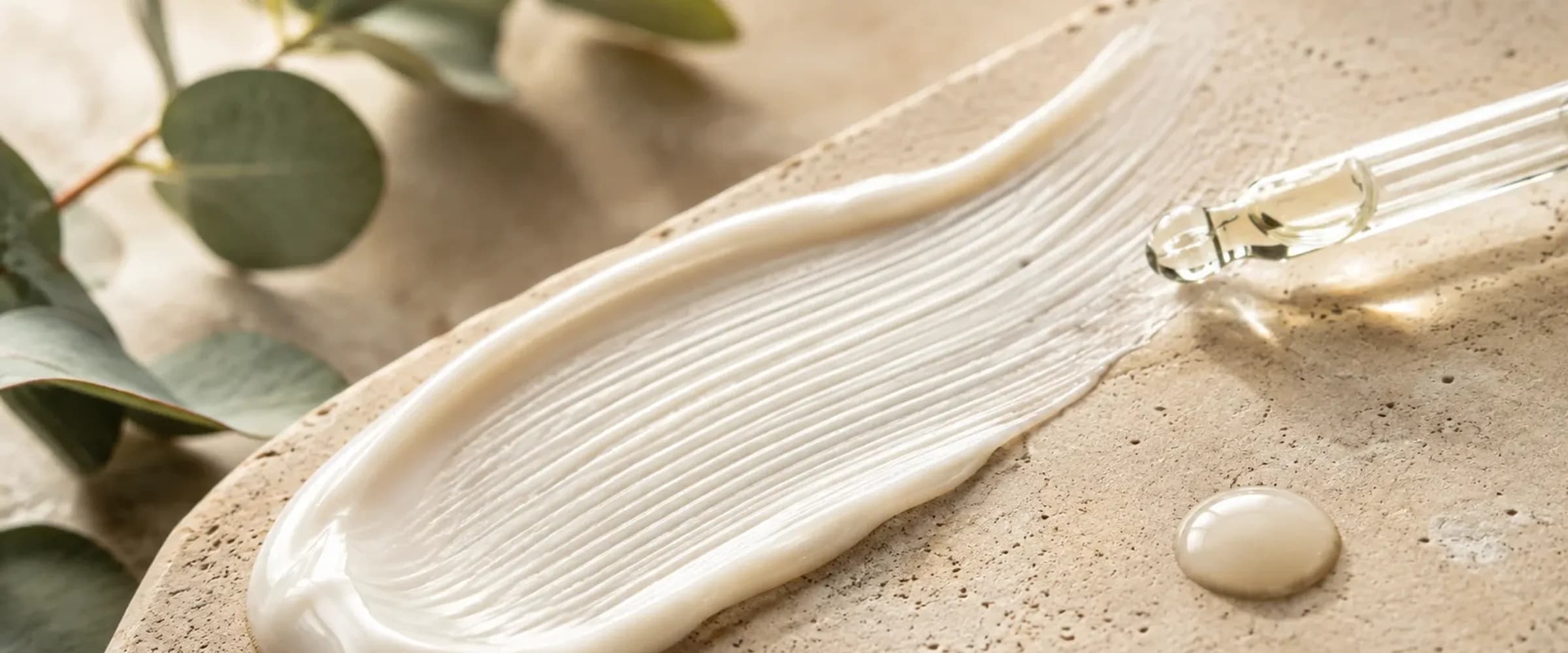 A rich cream stroked across a stone plate beside a glass dropper and eucalyptus